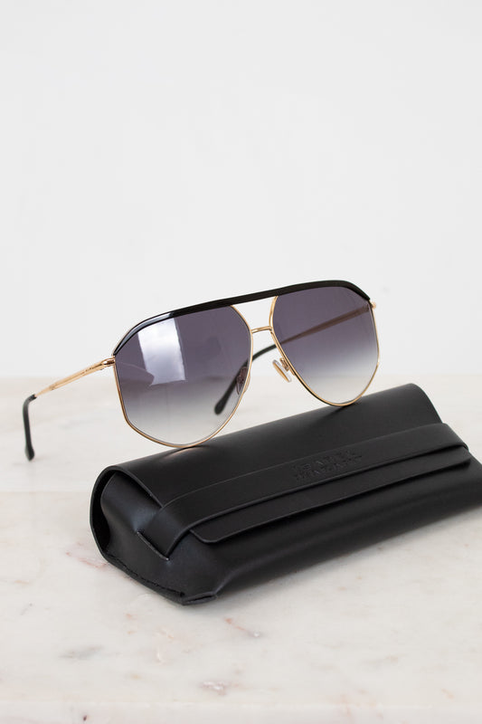 Sunglasses with gold frame and gradient lenses on a white surface with black case.