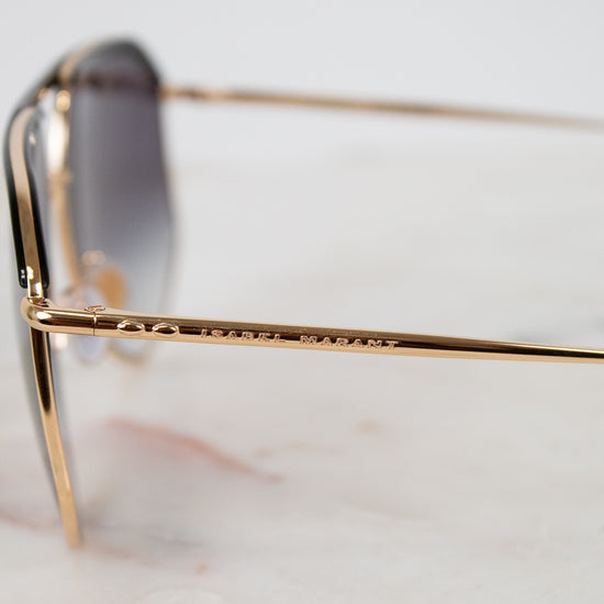 Gold-framed sunglasses with "Isabel  Marant" branding on a blurred background