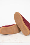 A pair of maroon suede shoes shown from the bottom, highlighting the tan textured rubber soles, set against a clean white background.