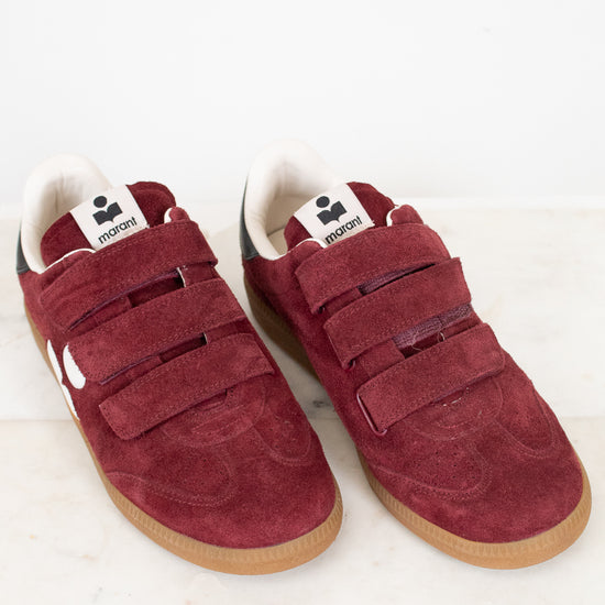 A pair of vintage maroon suede sneakers with triple Velcro straps, white lining, and gum soles, displayed on a light marble surface against a white background.