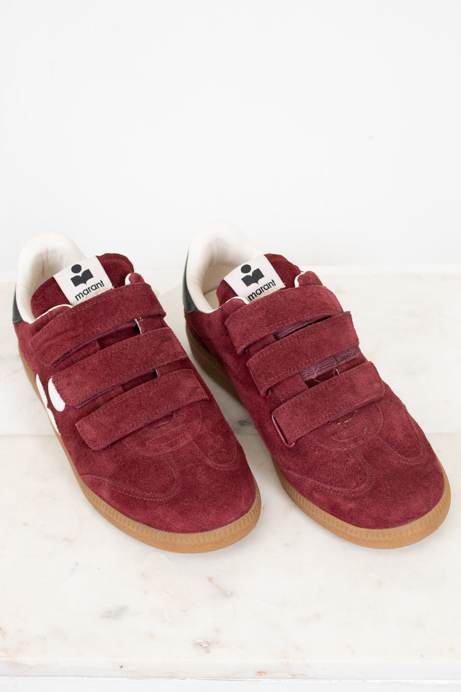 A pair of vintage maroon suede sneakers with triple Velcro straps, white lining, and gum soles, displayed on a light marble surface against a white background.