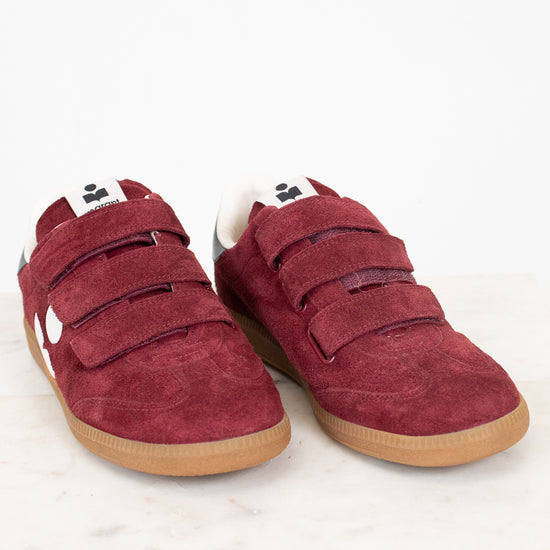 A pair of maroon suede shoes with triple Velcro straps and gum soles, displayed on a light marble surface against a white background.
