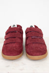 A pair of maroon suede sneakers with triple Velcro straps and gum soles, photographed from the front on a light marble surface against a white background.