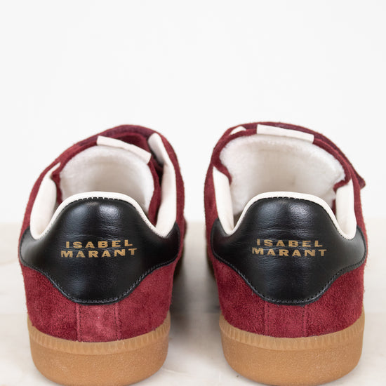 A pair of Isabel Marant sneakers shown from the back, featuring burgundy suede and black leather details with gold lettering, white lining, and tan rubber soles, set against a clean white background.