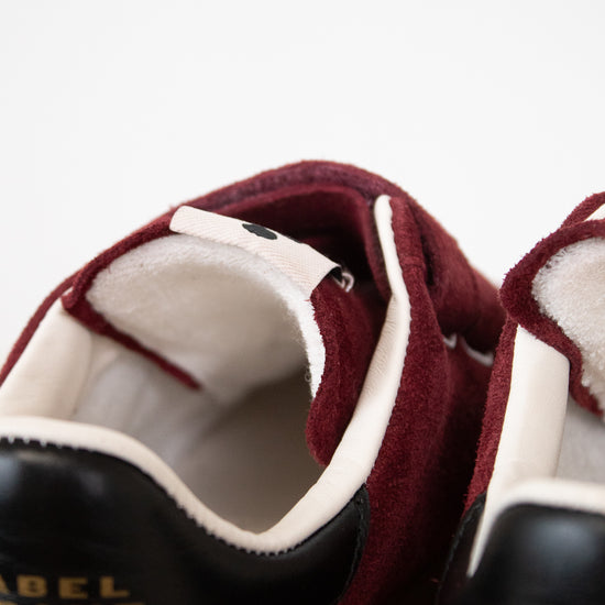Close-up of a pair of suede sneakers in burgundy and black with white lining and gold 'ISABEL MARANT' branding on the tongue.