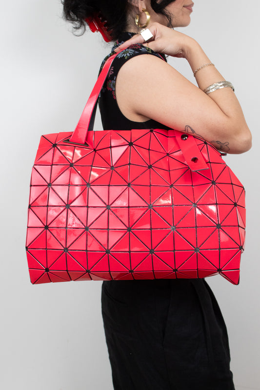 Woman wearing black outfit holding a hot pink puzzle-like detail tote bag on her shoulder and standing against a white background