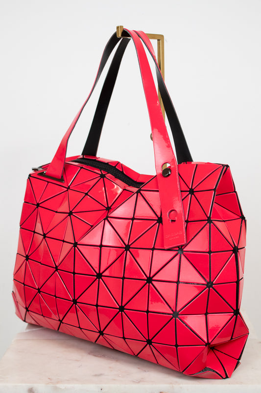 Abstract puzzle-like hot pink and black tote bag displayed on a gold stand against a white background
