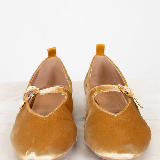 Pair of mustard yellow shoes with a strap on a light background