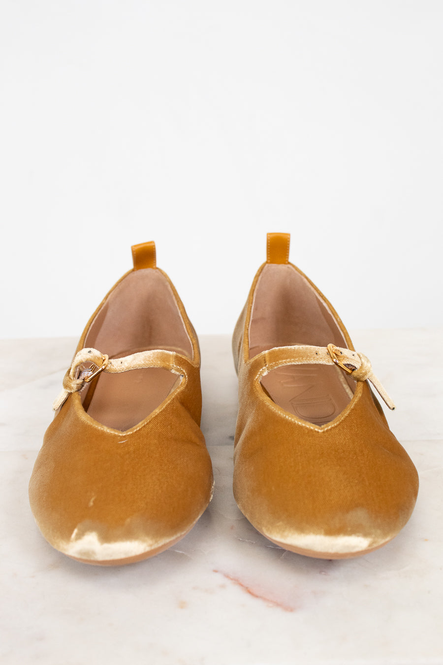 Pair of mustard yellow shoes with a strap on a light background