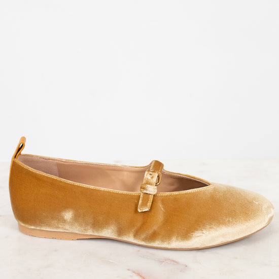 Gold velvet flat shoe with a gold buckle on a light gray background