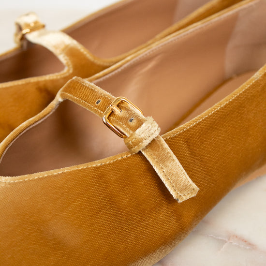 Pair of mustard yellow velvet shoes with a strap on a light background