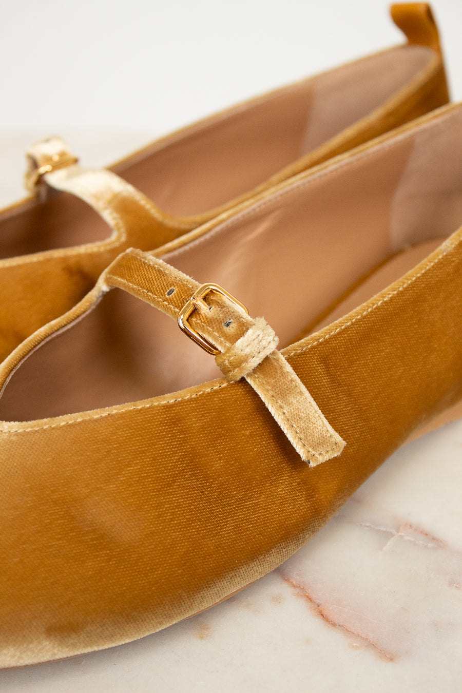 Pair of mustard yellow velvet shoes with a strap on a light background