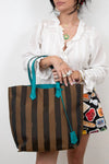 Person holding a striped bag with teal handles against a white background