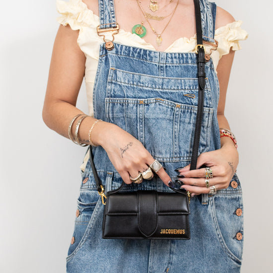 Person wearing denim overalls holding a black handbag with visible branding.