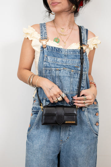 Person wearing denim overalls holding a black handbag with visible branding.