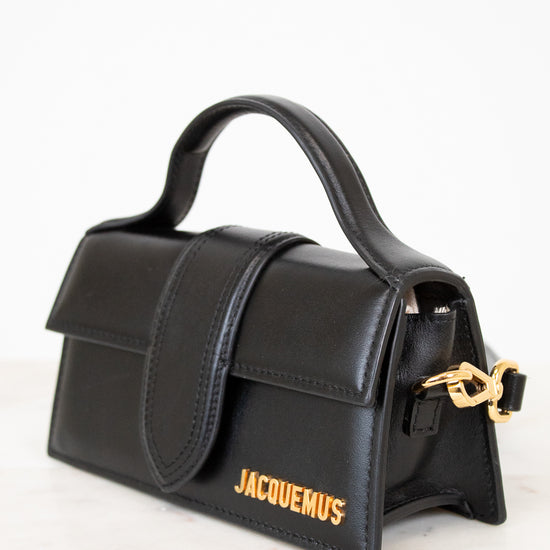 Black handbag with gold clasp and 'Jacquemus' branding on a white background