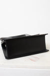 Bottom view of a black leather bag with a structured rectangular shape, resting on a white marble surface against a white background.