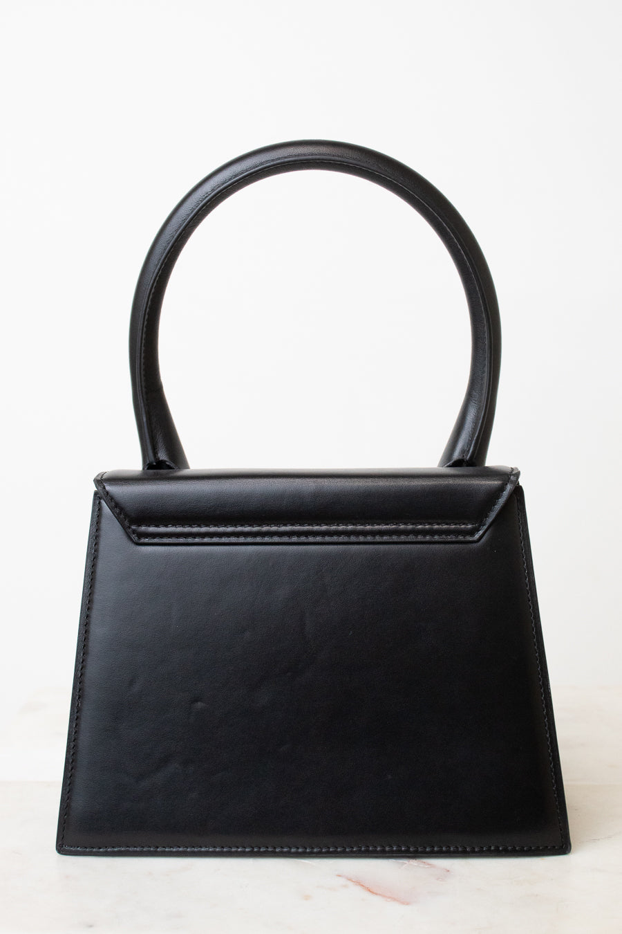 A black leather handbag with a structured, geometric shape and a single integrated top handle, photographed against a clean white background.
