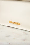 White clutch bag with gold 'Jacquemus' logo on a marble surface
