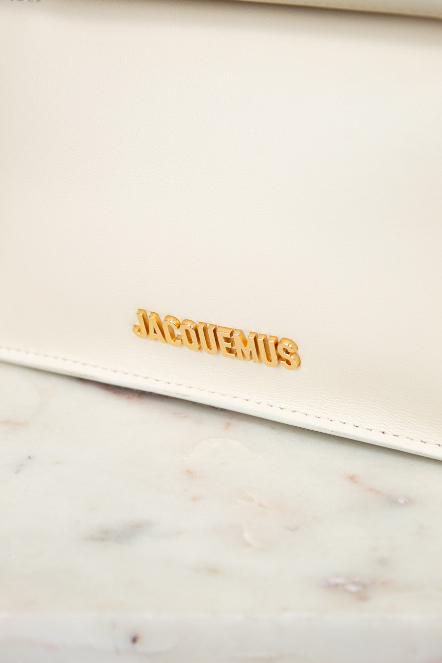 White clutch bag with gold 'Jacquemus' logo on a marble surface