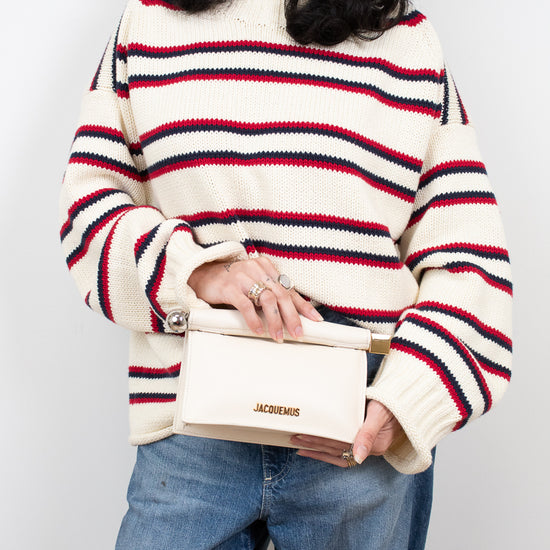 Person wearing a striped sweater and holding a white handbag against a plain background