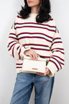 Person wearing a striped sweater and holding a white handbag against a plain background