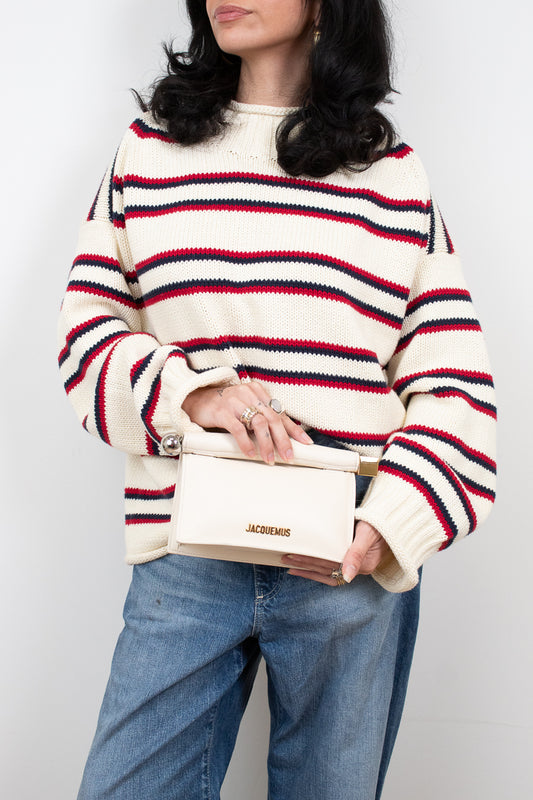 Person wearing a striped sweater and holding a white handbag against a plain background