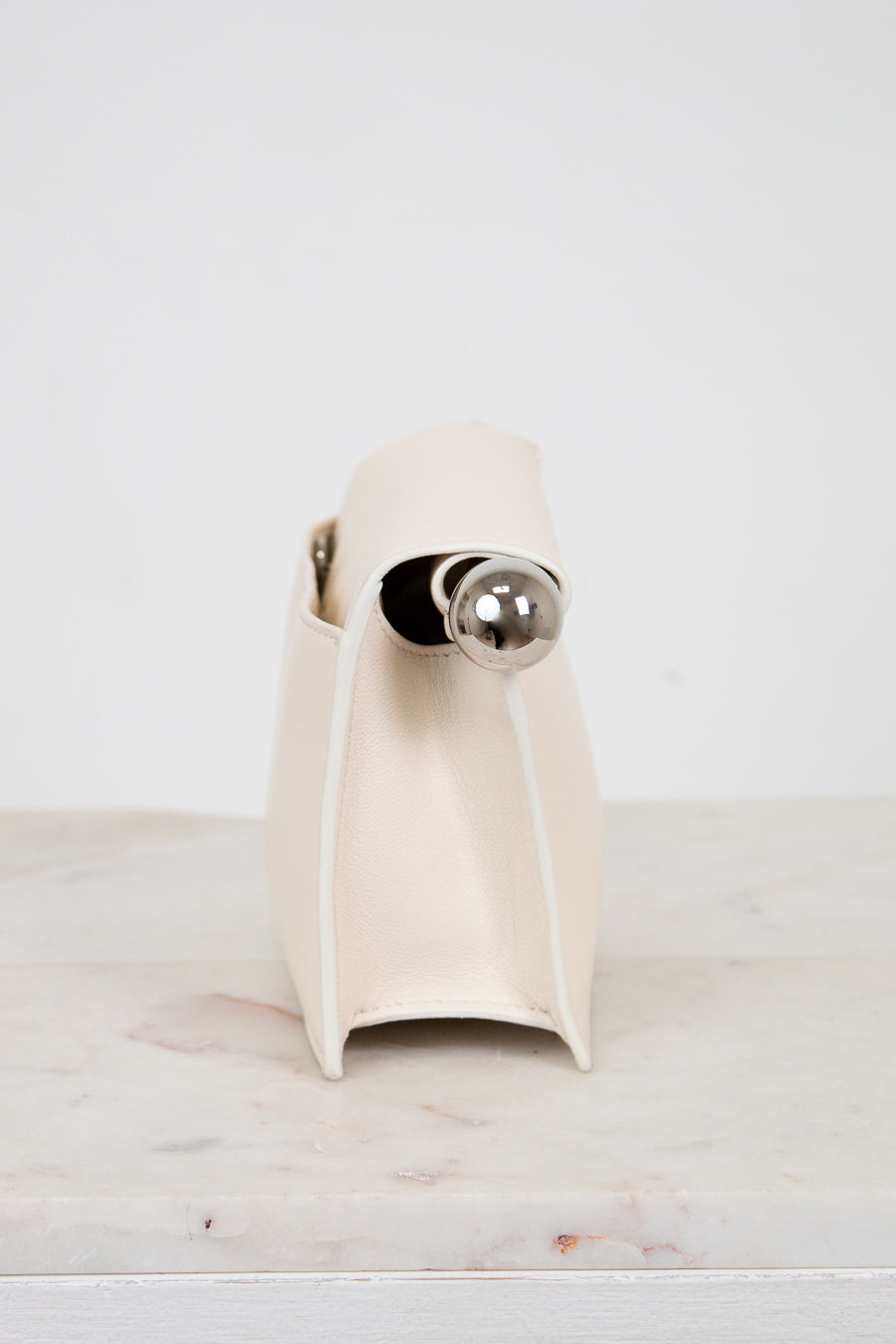 White side profile of clutch with a silver accent on a light marble surface.