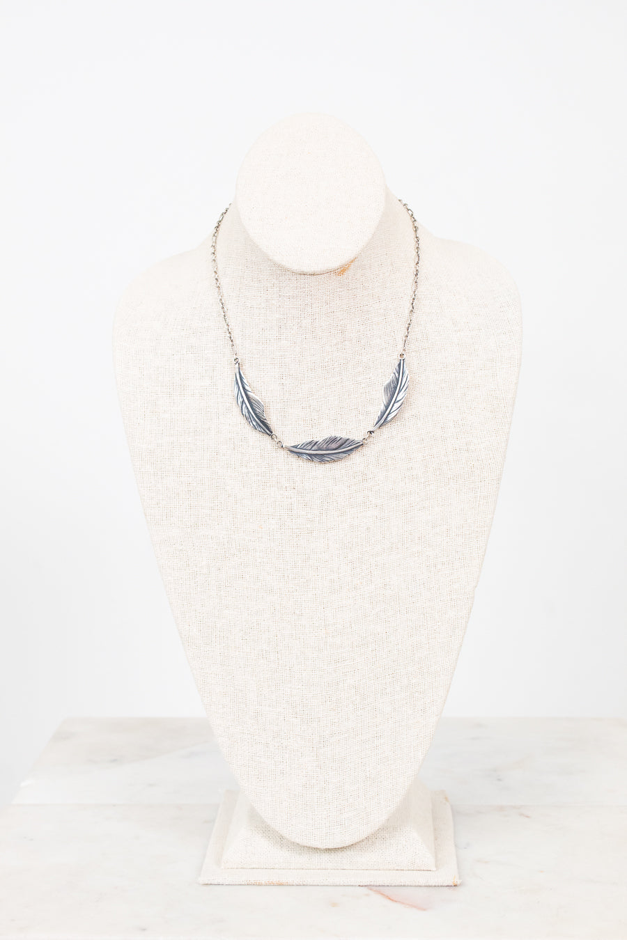 Feather necklace on a mannequin bust against a white background