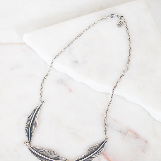 Silver feather necklace on a marble surface