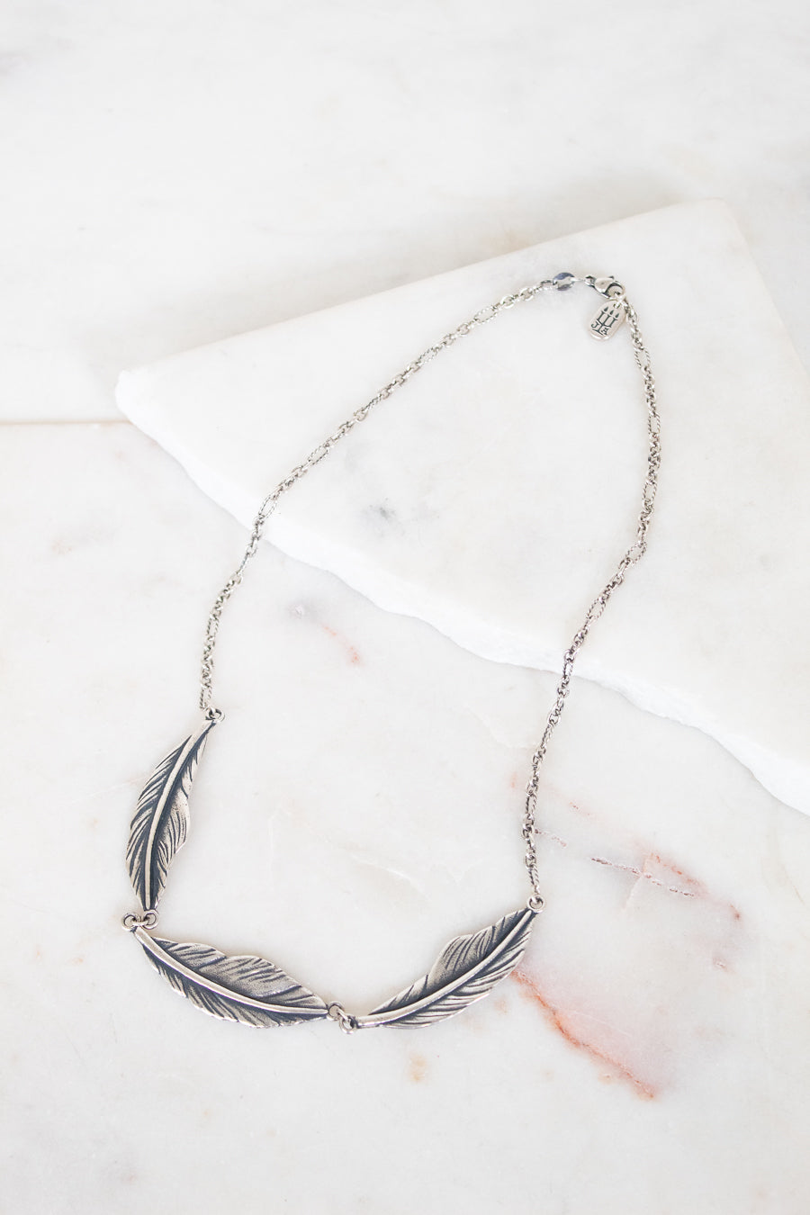 Silver feather necklace on a marble surface