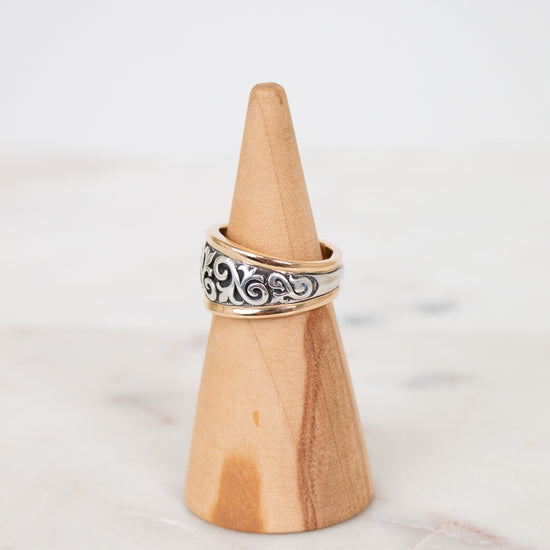 Wooden ring holder with a silver ring on a marble surface