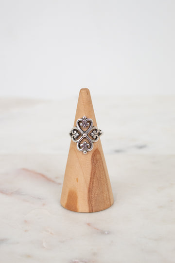 Silver ring with a decorative design on a wooden cone against a light background