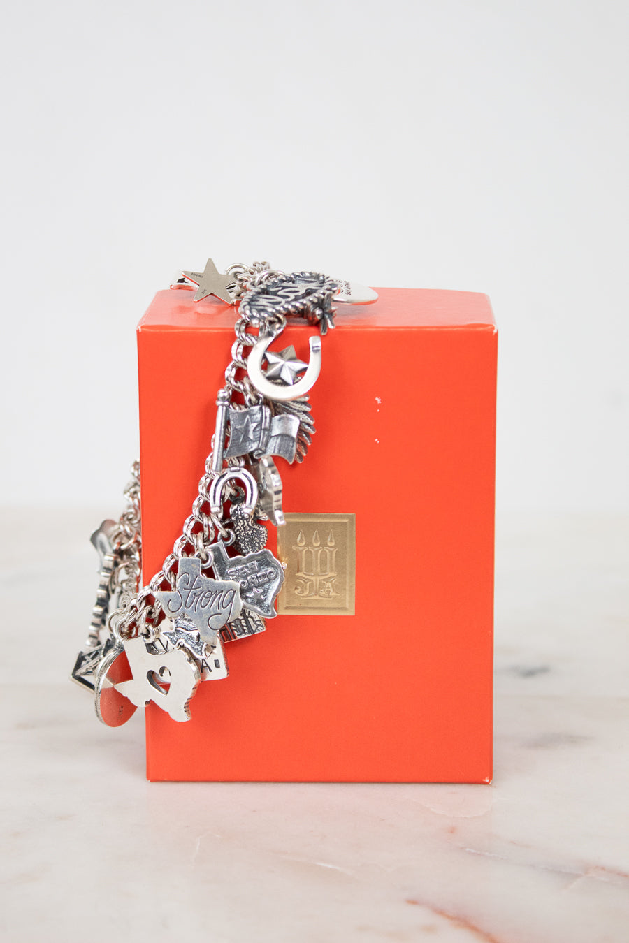 Silver charm bracelet on an orange box with a marble surface