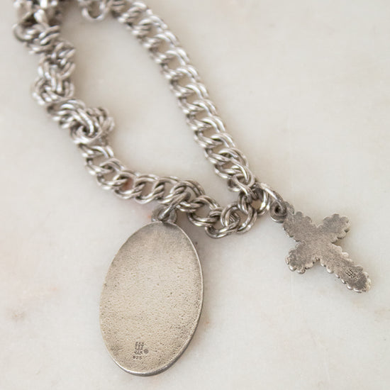 Silver chain bracelet with a round pendant and cross charm on a light background