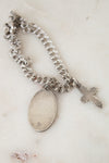 Silver chain bracelet with a round pendant and cross charm on a light background
