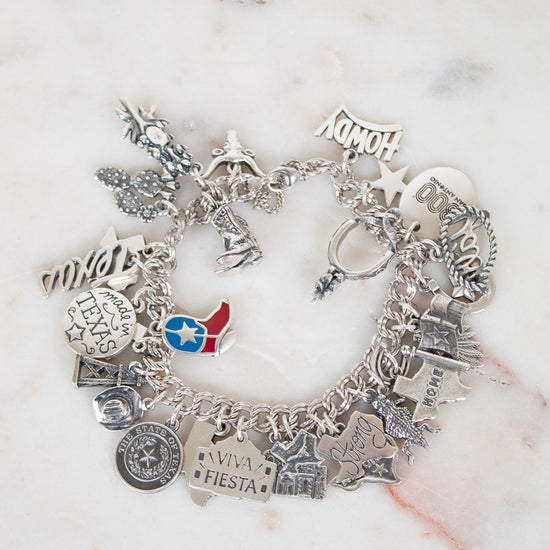 Silver charm bracelet with various charms on a marble surface