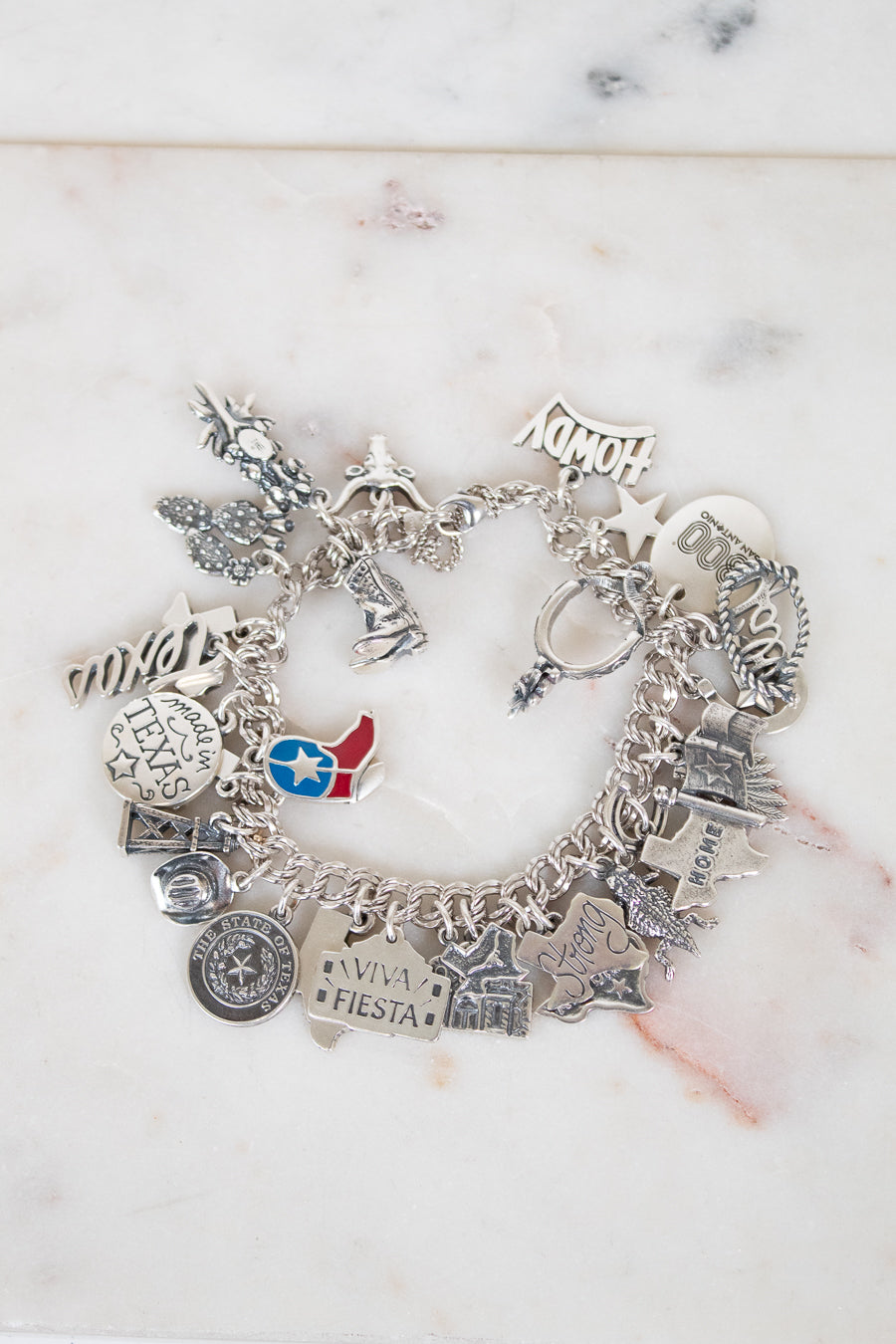 Silver charm bracelet with various charms on a marble surface