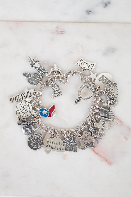 Silver charm bracelet with various charms on a marble surface
