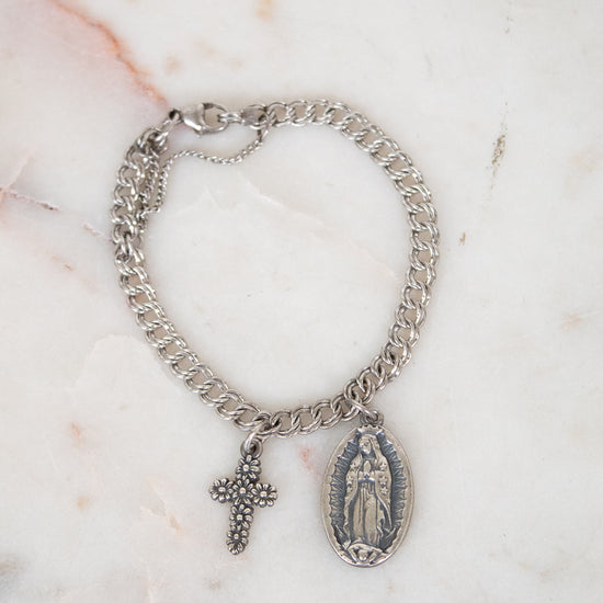 Silver chain bracelet with a cross and religious charm on a marble surface