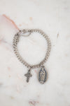 Silver chain bracelet with a cross and religious charm on a marble surface