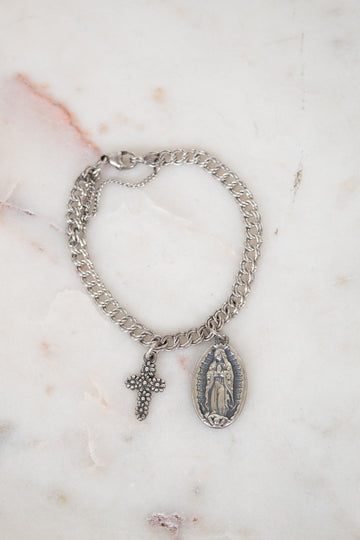 Silver chain bracelet with a cross and religious charm on a marble surface