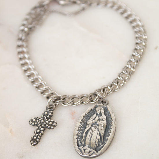 Silver bracelet with a cross and religious charm on a marble surface