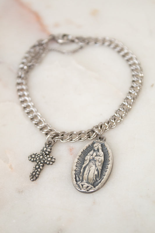 Silver bracelet with a cross and religious charm on a marble surface