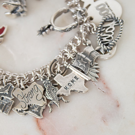 Silver charm bracelet with various charms on a marble surface