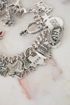 Silver charm bracelet with various charms on a marble surface