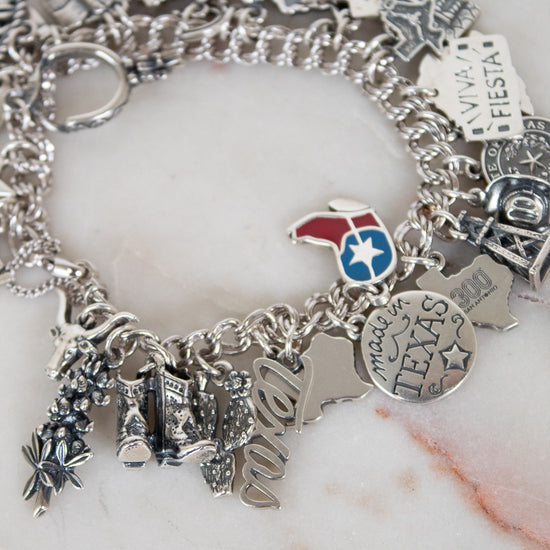 Silver charm bracelet with various charms on a marble surface