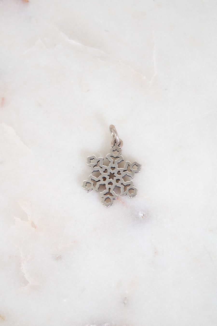 Silver snowflake pendant on a white marble background