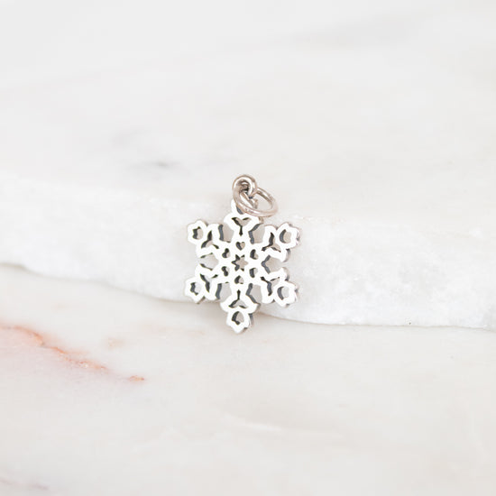Silver snowflake charm on a white marble surface