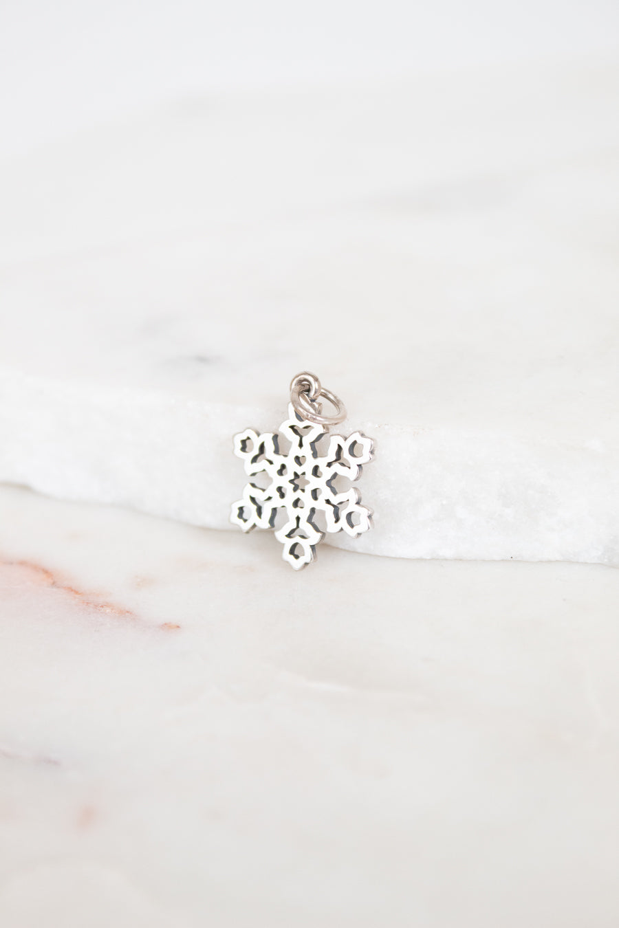 Silver snowflake charm on a white marble surface